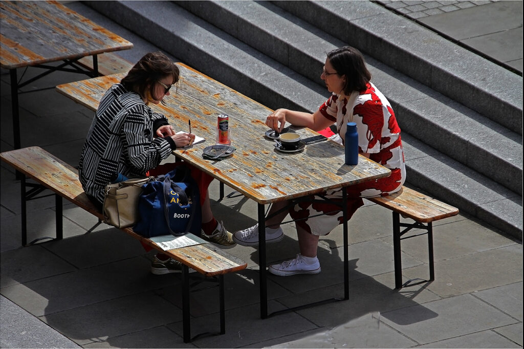 Two women sitting at table working in open air.